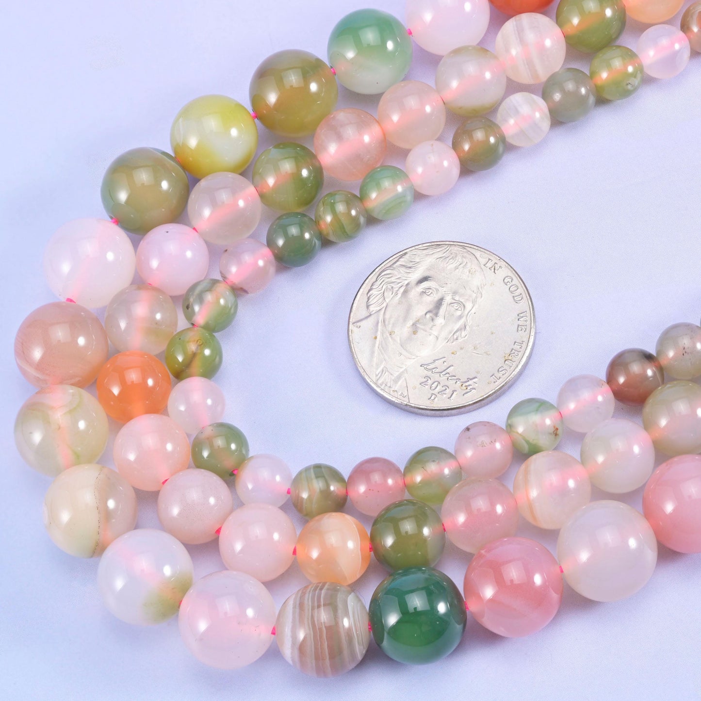 Multicolored round beads with a coin for size comparison on a light purple background